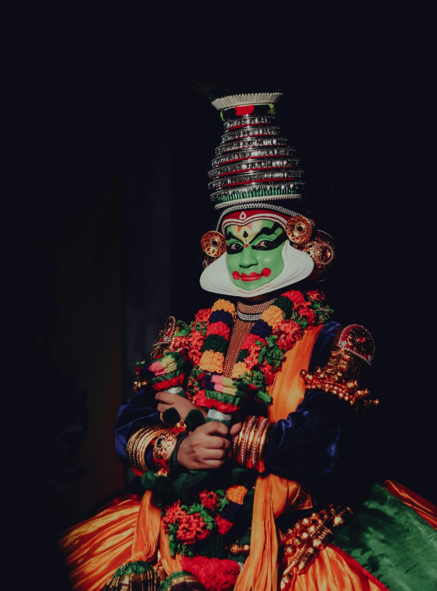 Traditional Kathakali dancer from Kerala, India, wearing elaborate green face makeup, ornate headgear, and colorful ceremonial costume.