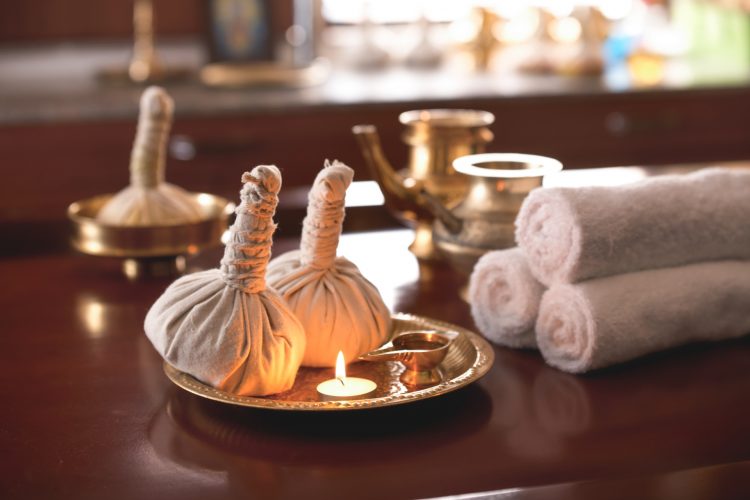 Traditional Panchakarma therapy setup with herbal bolus, brass vessels, oil lamp, and rolled towels