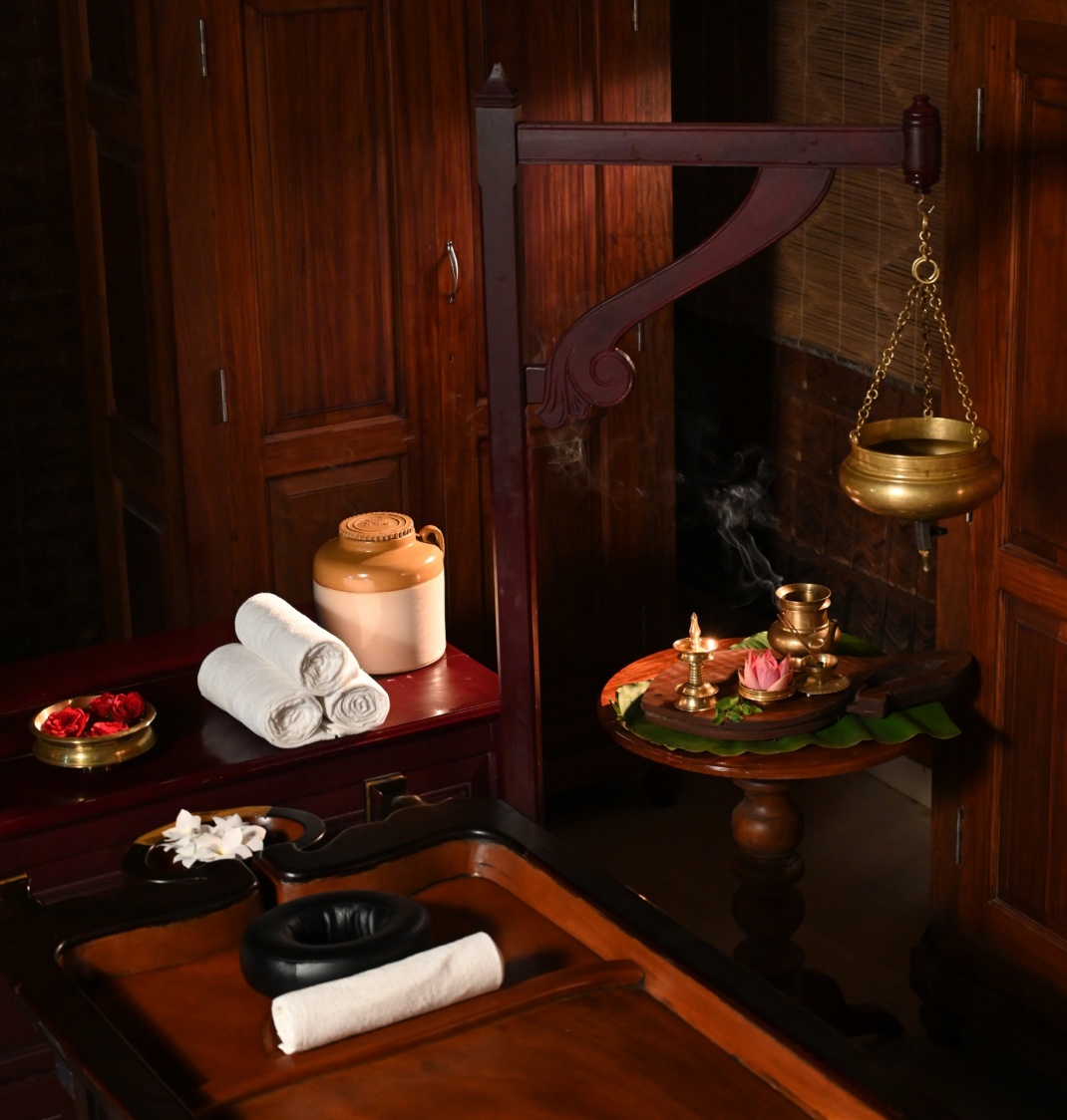 Traditioneller ayurvedischer Therapieraum mit Holzmöbeln, Messinggefäß für Öl und Kräuteraufbau
